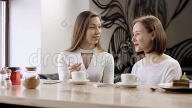 两个年轻的女人坐在咖啡馆里聊天。 这是一次<strong>朋友聚会</strong>。 女孩们坐在餐桌旁的咖啡馆里
